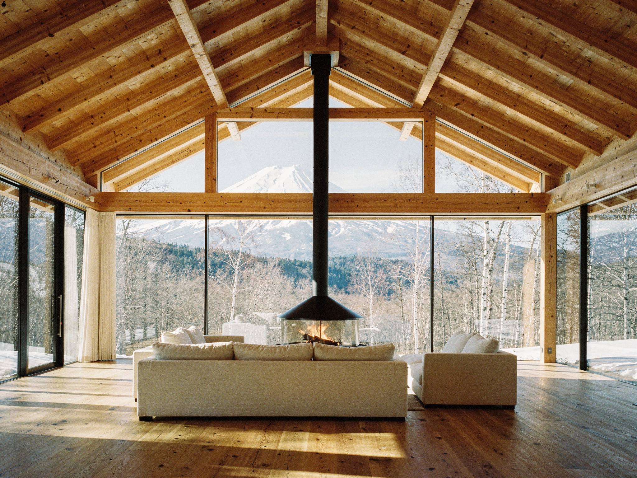 Double-height lounge under the glulam gable, suspended fire, mountain view in bright daylight