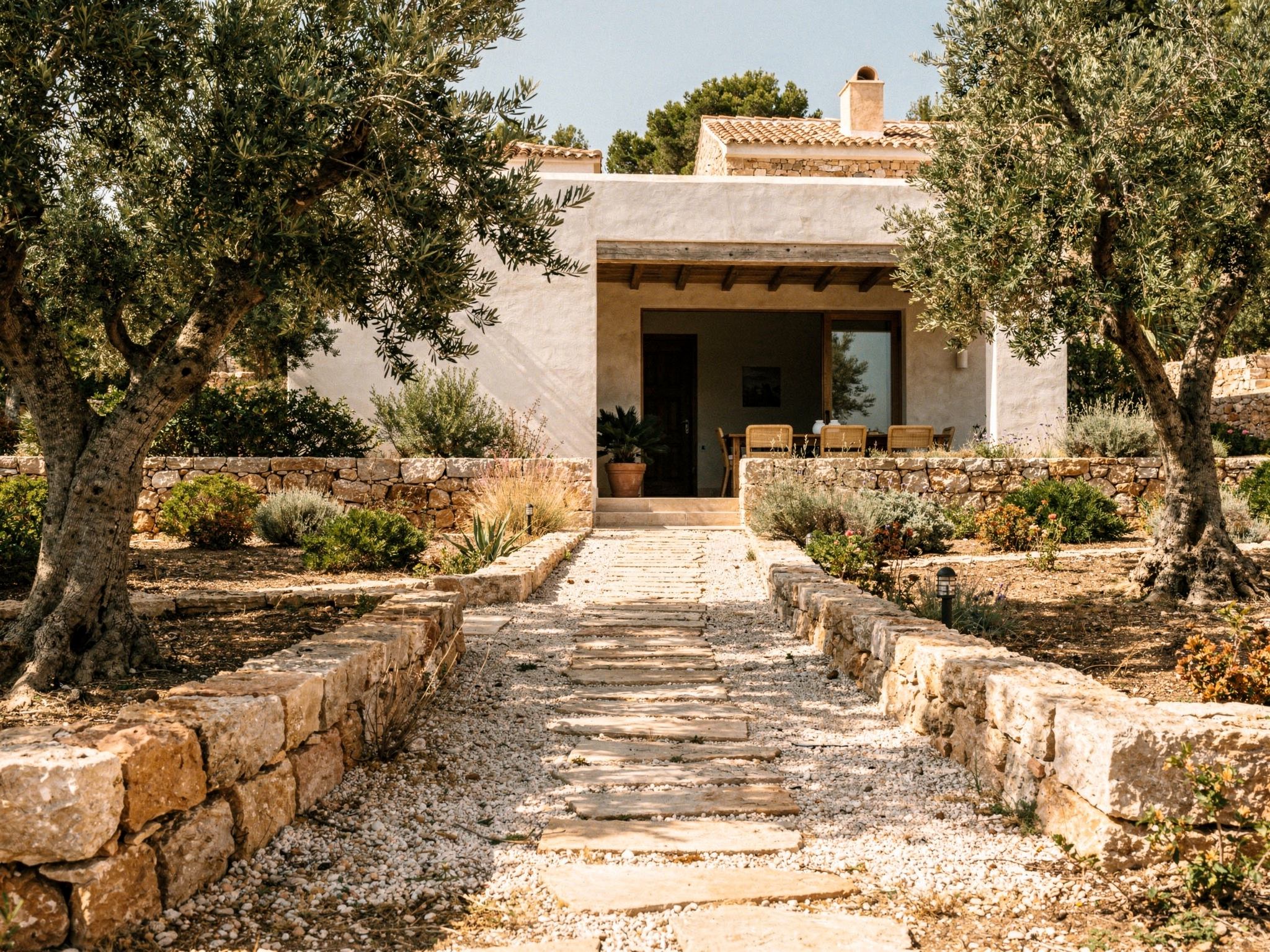 A gravel path through olive trees to a shaded entrance loggia