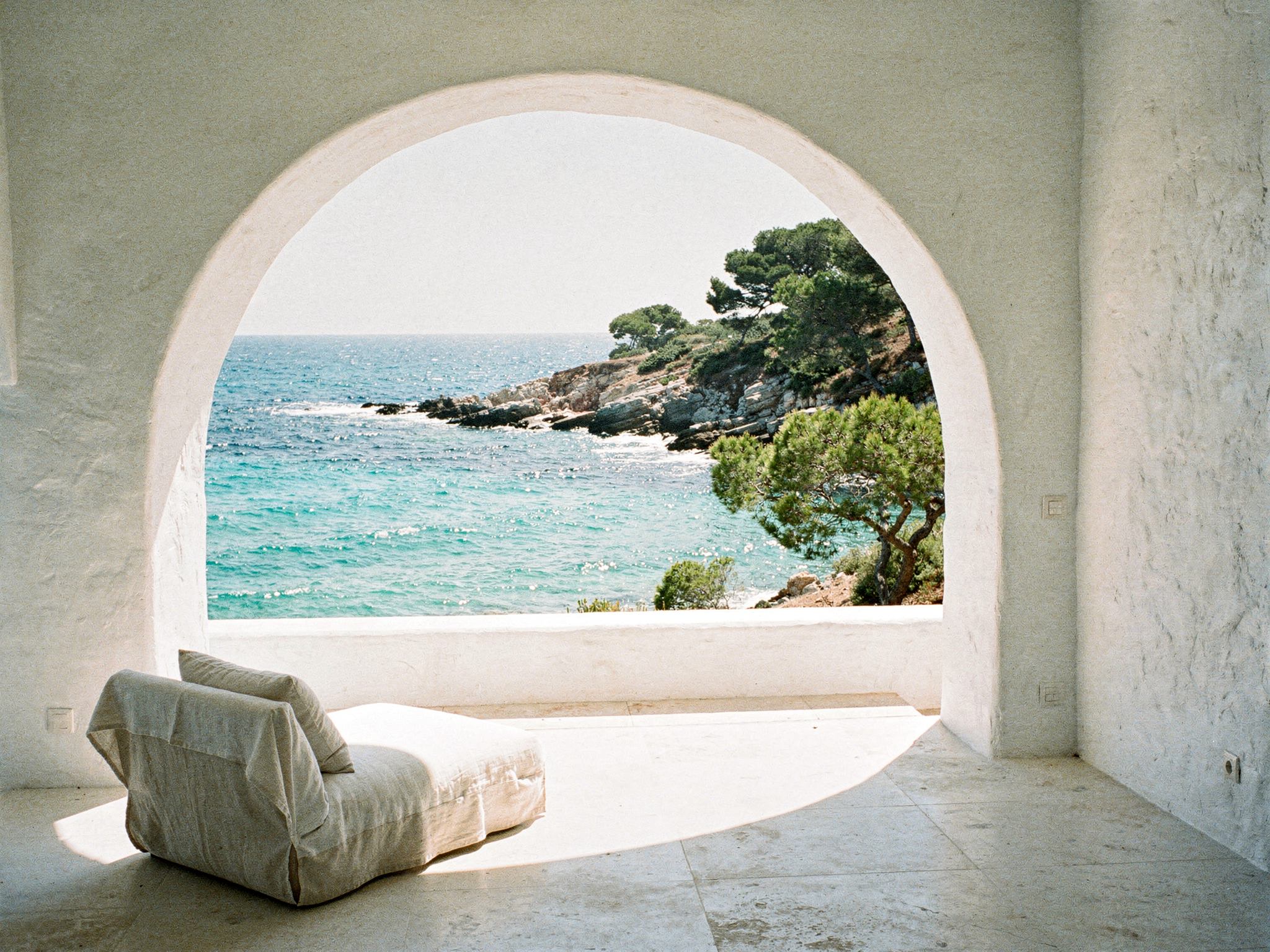 View through a deep arched loggia to the turquoise cove and pines