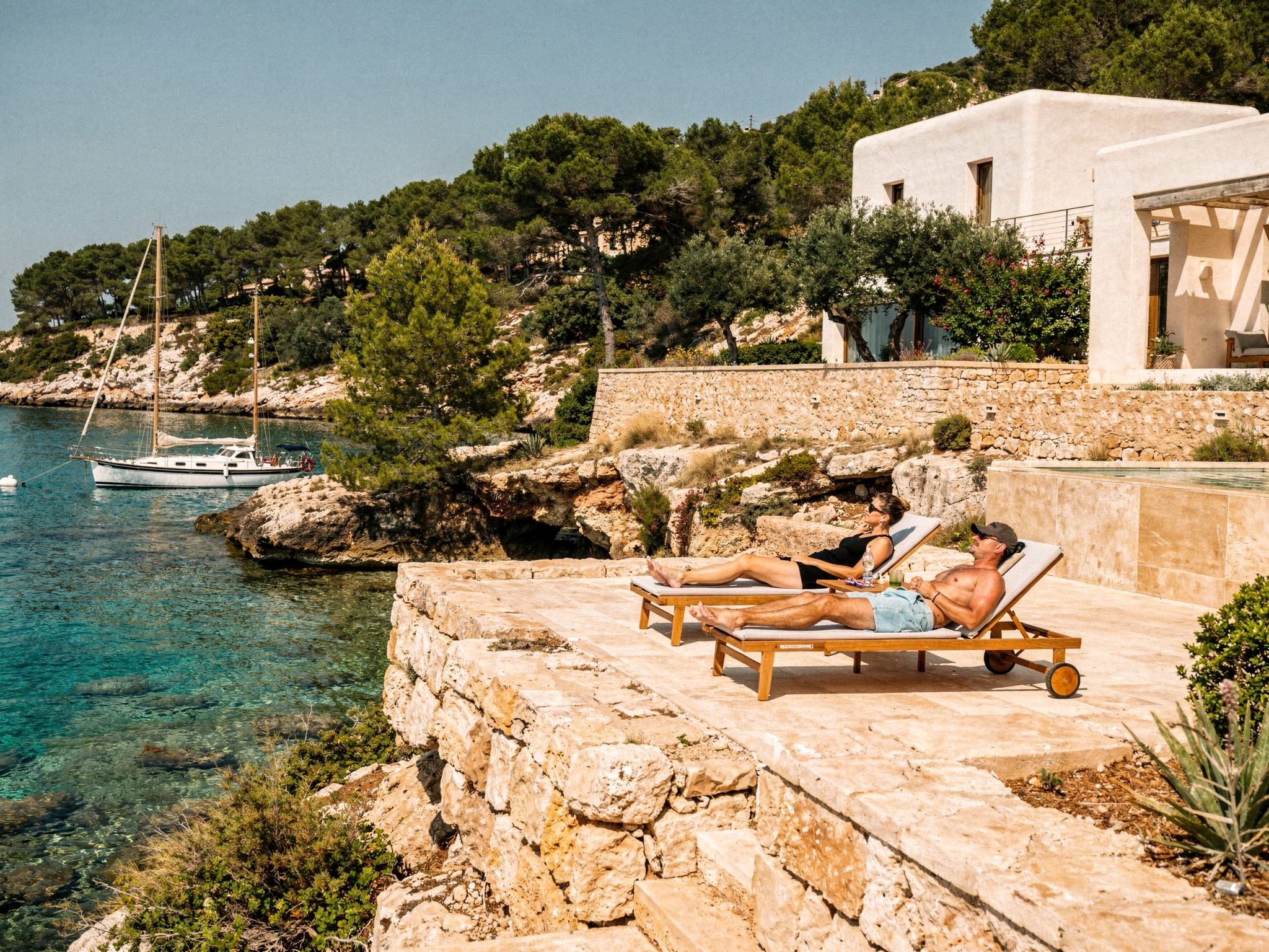 Guests relaxing by the stone pool with the turquoise cove behind