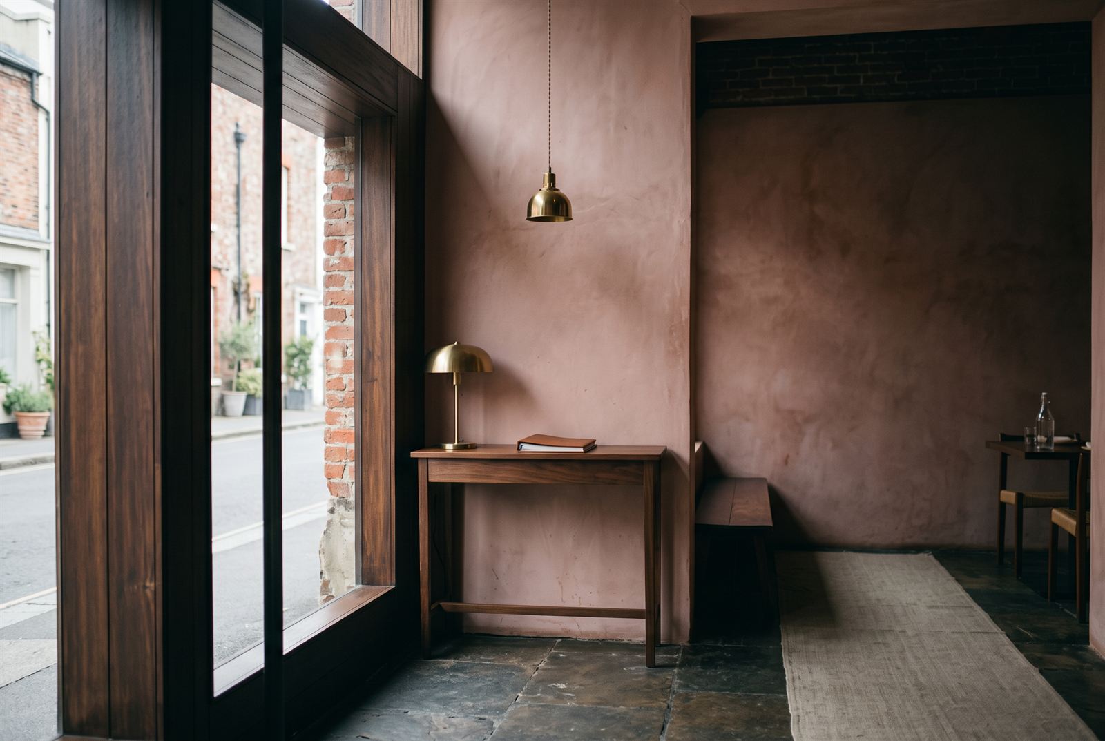 Entry threshold — walnut-framed glazing, rose plaster, a brass lamp and the reservations book on the host table