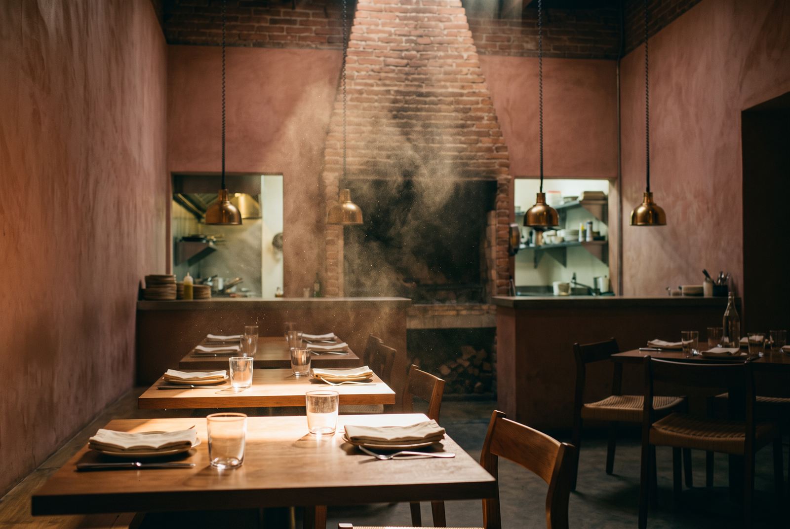 Morning light falling down the brick chimney through drifting woodsmoke, across empty set tables