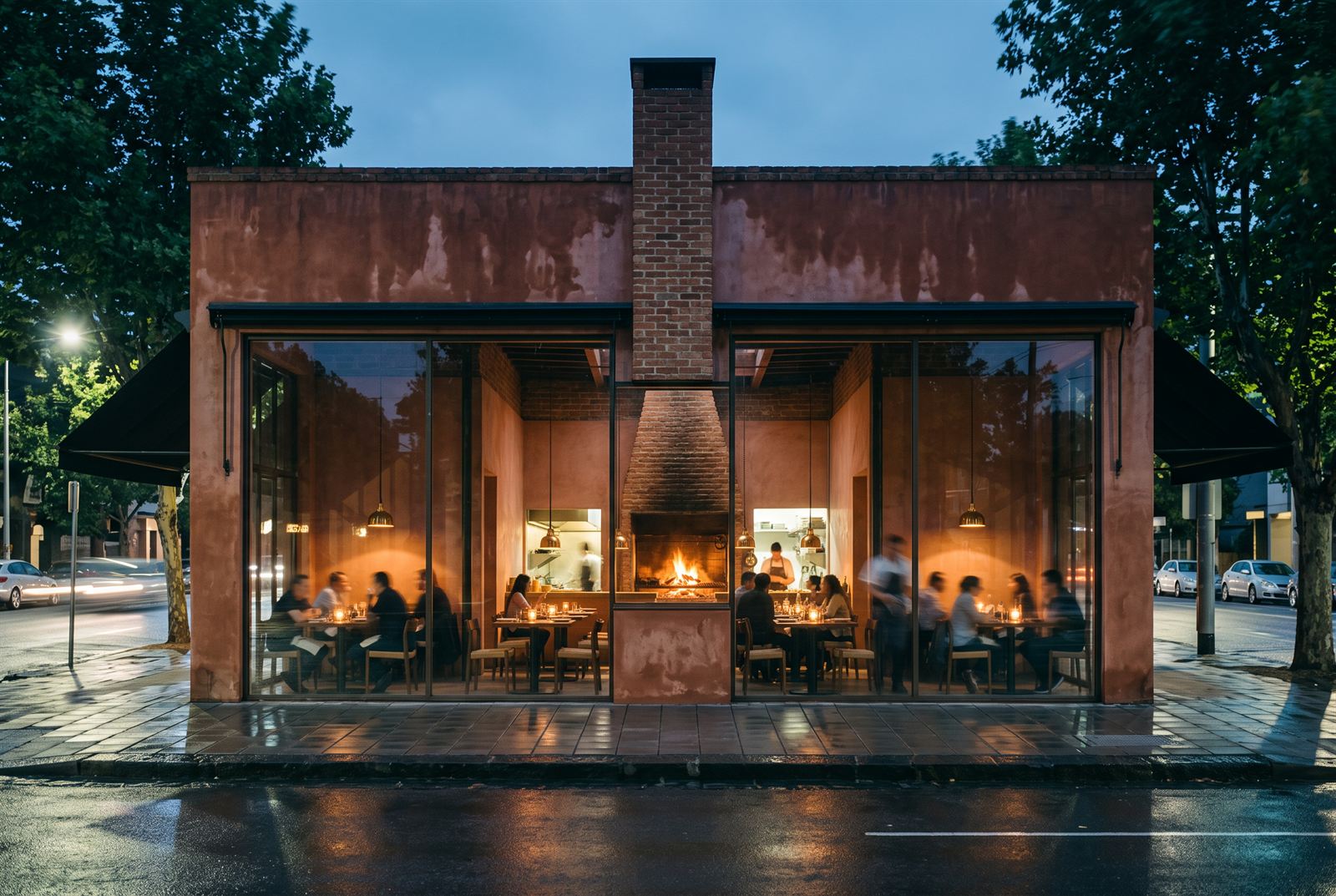 Ember Restaurant at dusk — the brick chimney splitting the glazed facade, the open fire glowing at the centre of the room