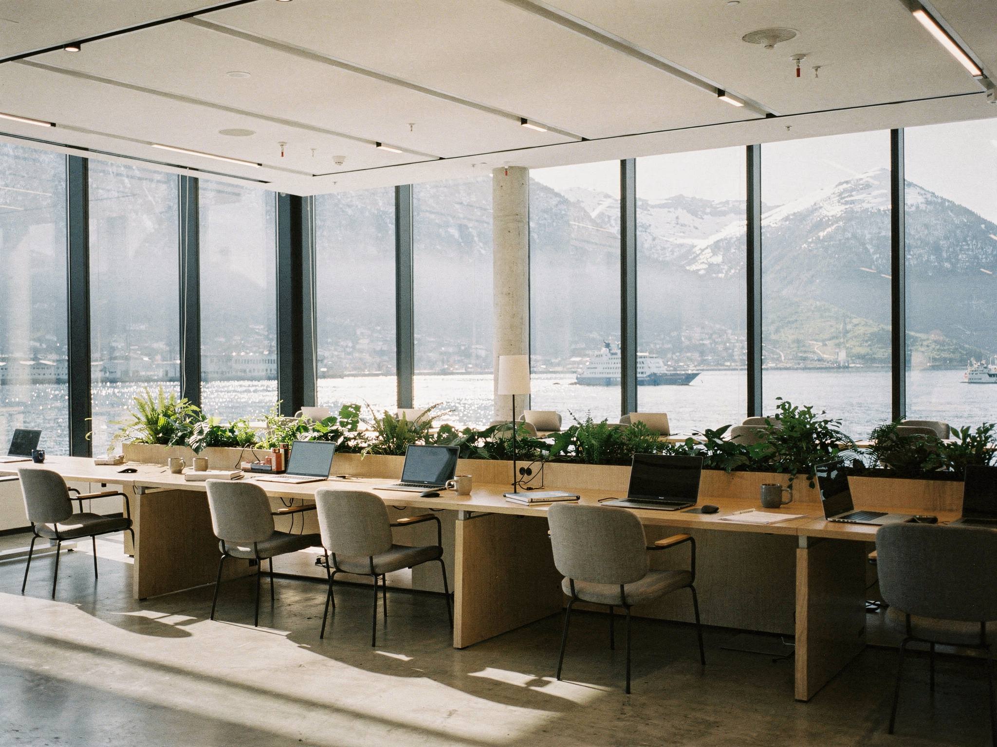 Open-plan office floor with oak desks and the mountains framed in glass
