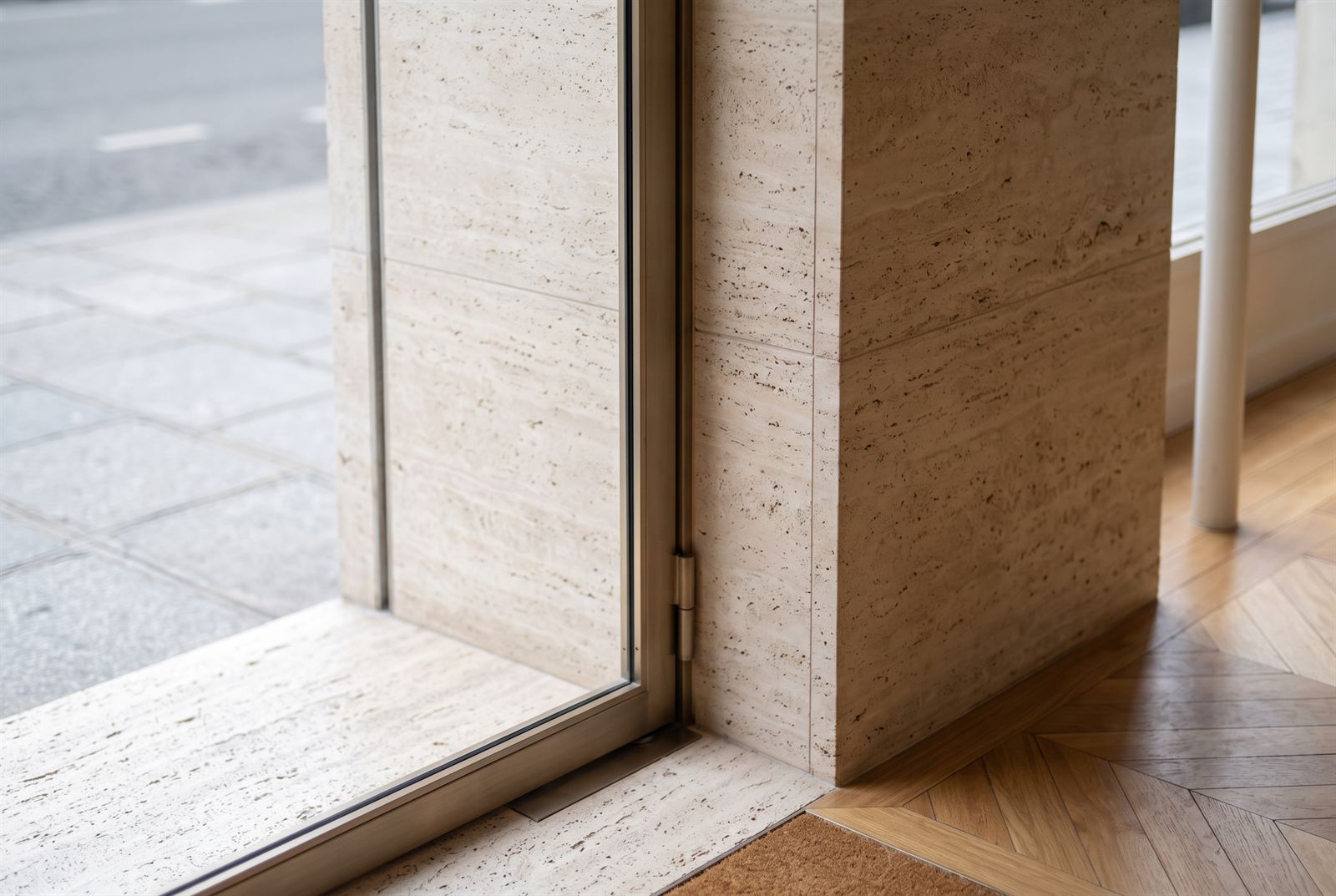 Entry threshold detail where the travertine portal, steel door frame and chevron oak floor meet