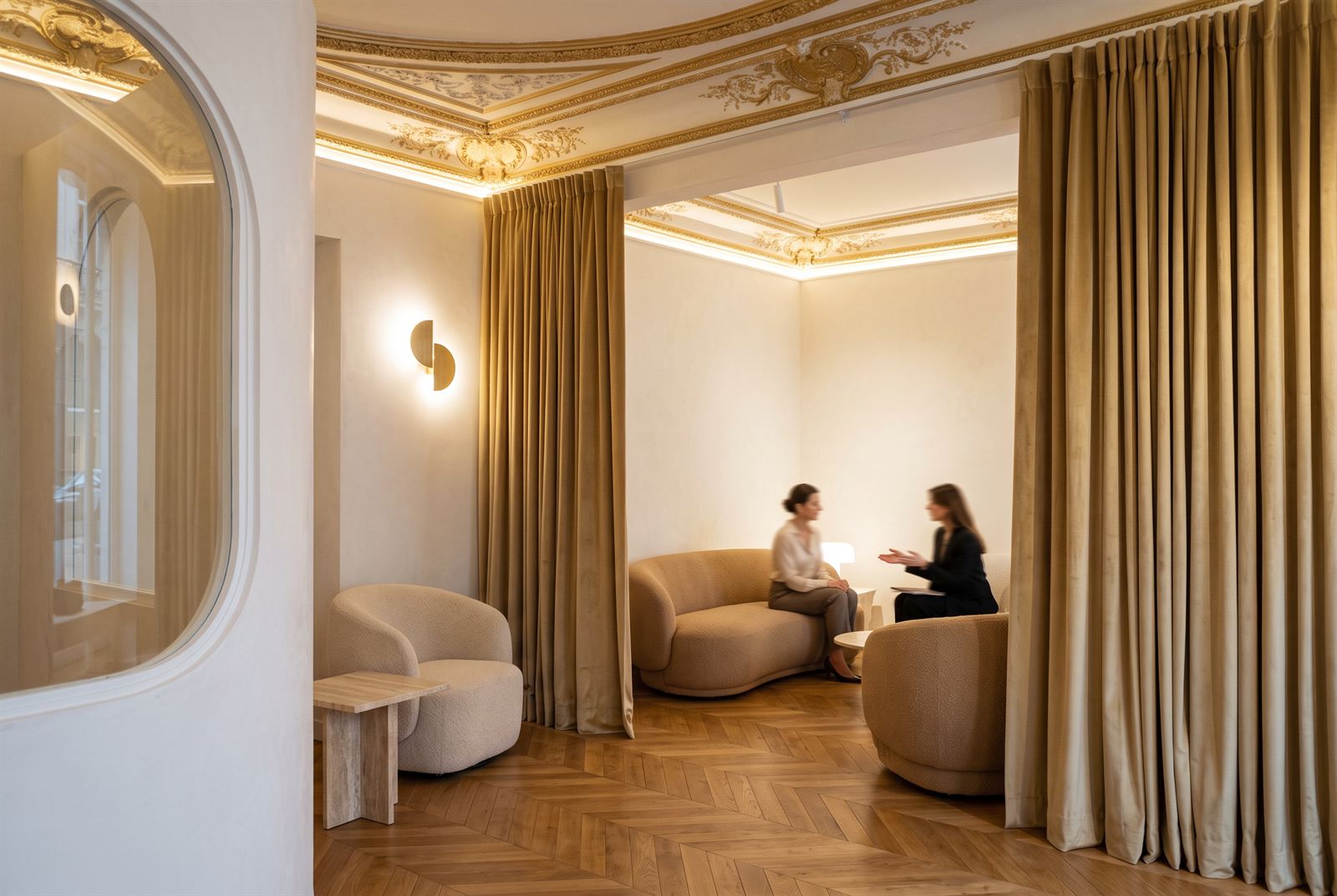 Fitting lounge with bouclé seating and velvet curtains under the gilded cornice, two women in conversation