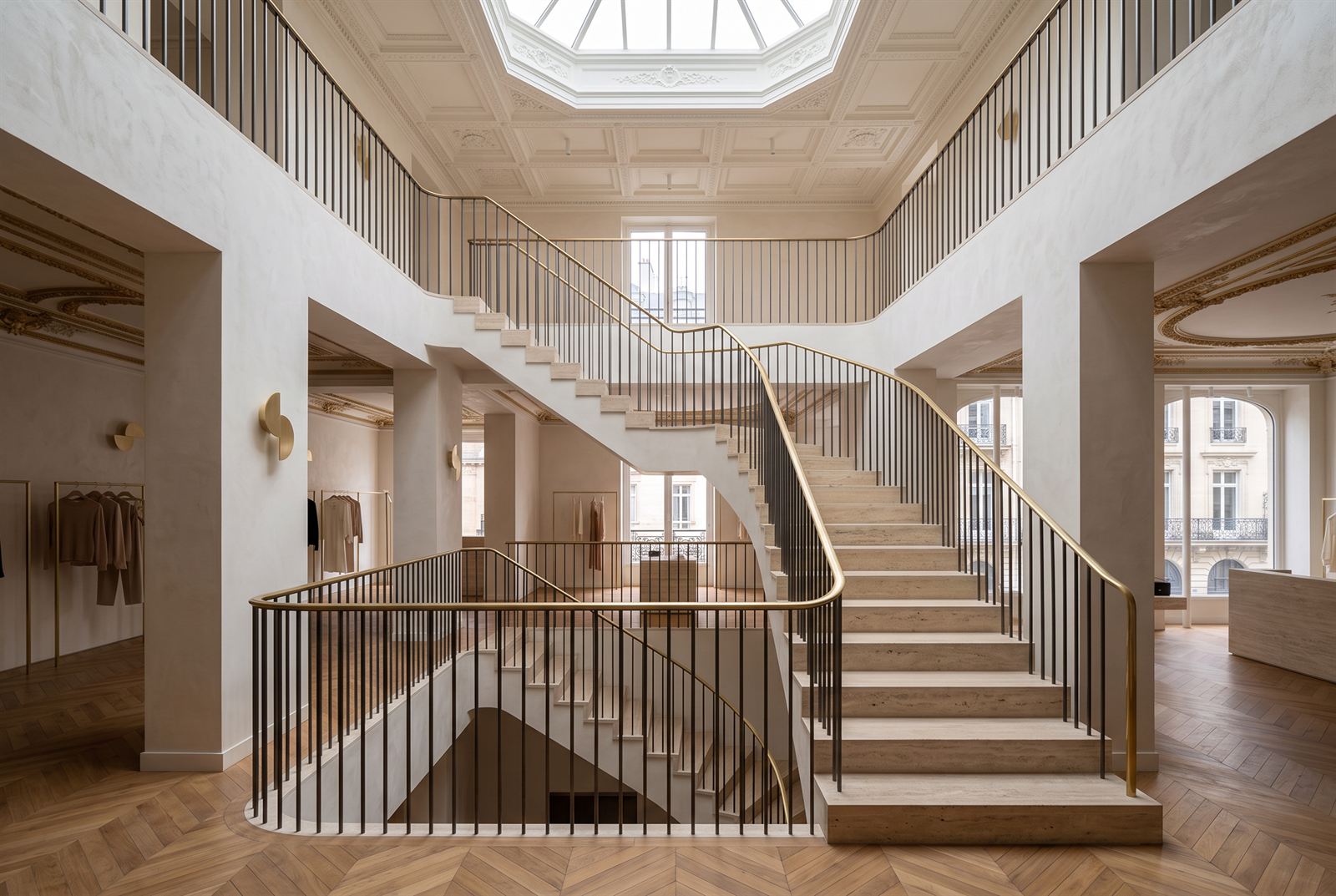 Double-height stair hall with travertine treads and a brass handrail rising beneath an octagonal rooflight