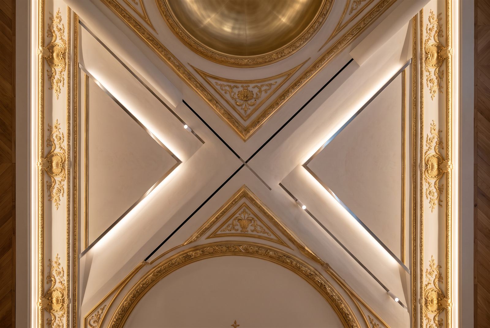 Looking straight up at the gilded ceiling where new recessed light coves cross the restored plasterwork
