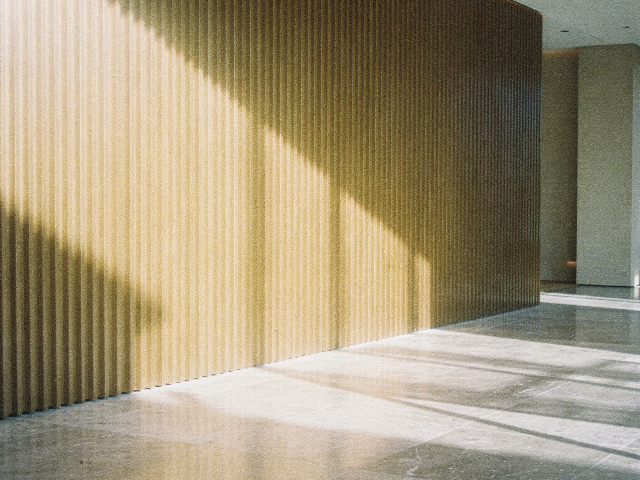 Daylight raking across bronze fins and a stone floor in a lobby
