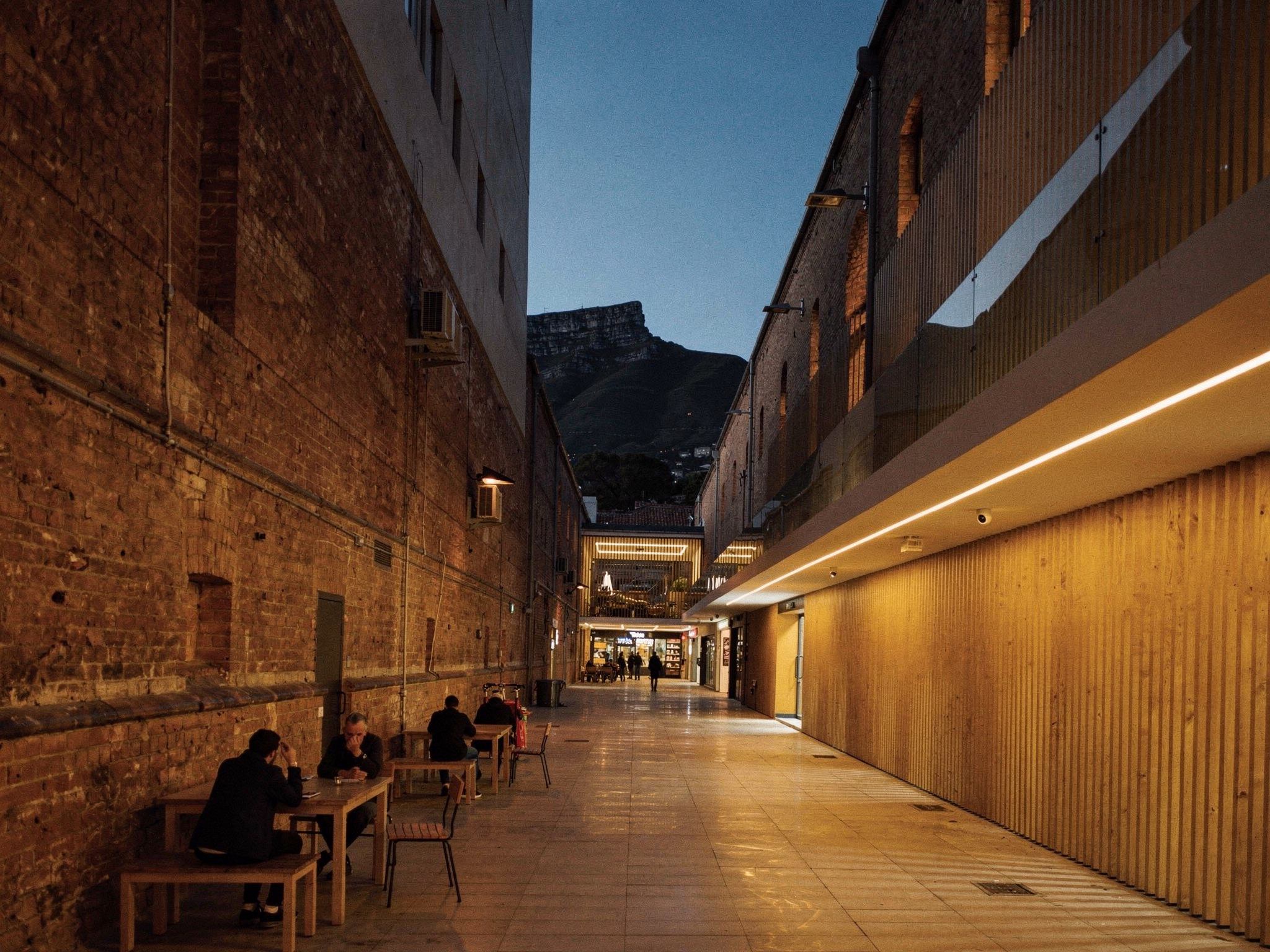 The lane at blue hour with every shopfront lit warm and the rooflights glowing above
